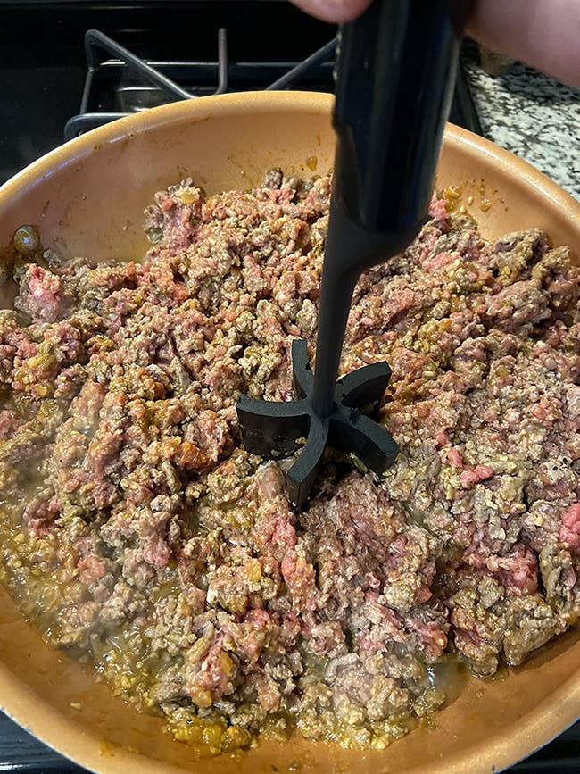 reviewer using the black masher to breakup a pan full of ground beef