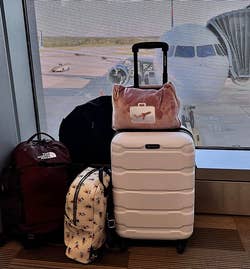 reviewer's pink blanket and pillow wrapped up in its carrying case and attached to the handle of their suitcase