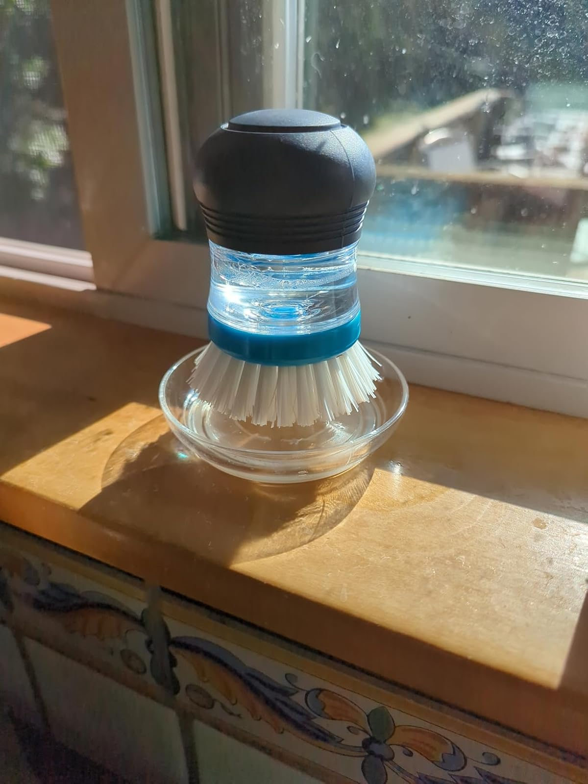Dish scrubber with a built-in soap dispenser connected  a windowsill