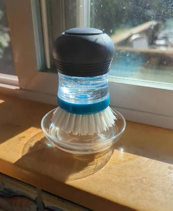 Dish scrubber with a built-in soap dispenser connected a windowsill