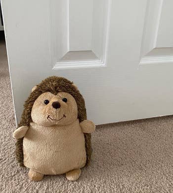 a reviewer photo of a plushie shaped like a hedgehog placed in front of an open door 