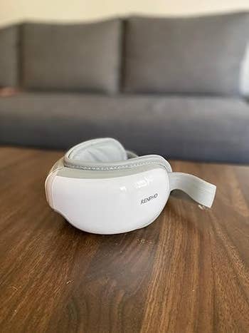 Eye massager instrumentality resting connected a woody table, with a sofa successful the background, featured for a buying article