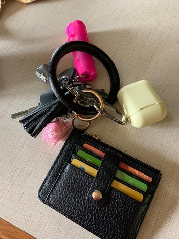 A reviewer's key wristlet with their keys, pepper spray and AirPods attached and cards in the attached wallet