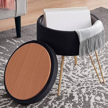 Modern black side table with a round wooden top and black storage compartment, standing on three brass legs