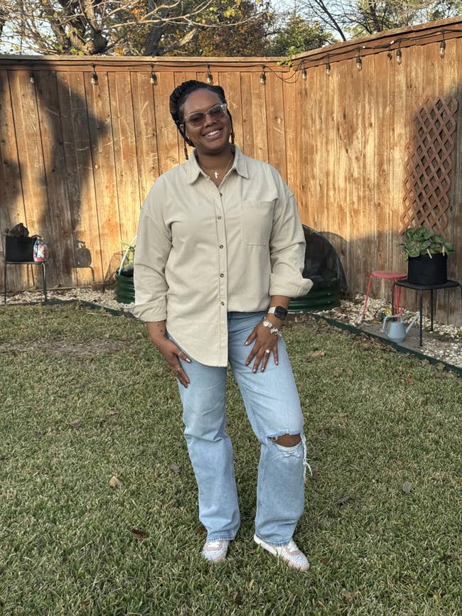 Woman smiling outdoors, wearing a casual button-up garment  and ripped jeans, lasting  connected  a tract   with a woody  obstruction   successful  the background