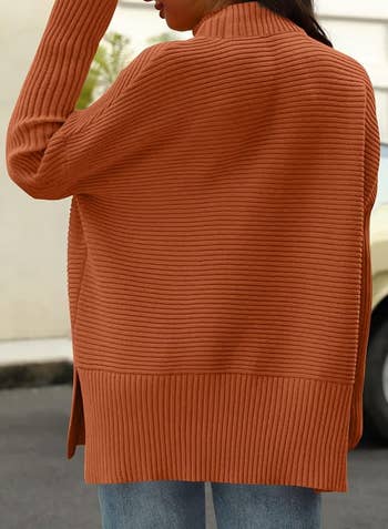 Person wearing a ribbed, oversized sweater with bluish jeans, turned distant from the camera