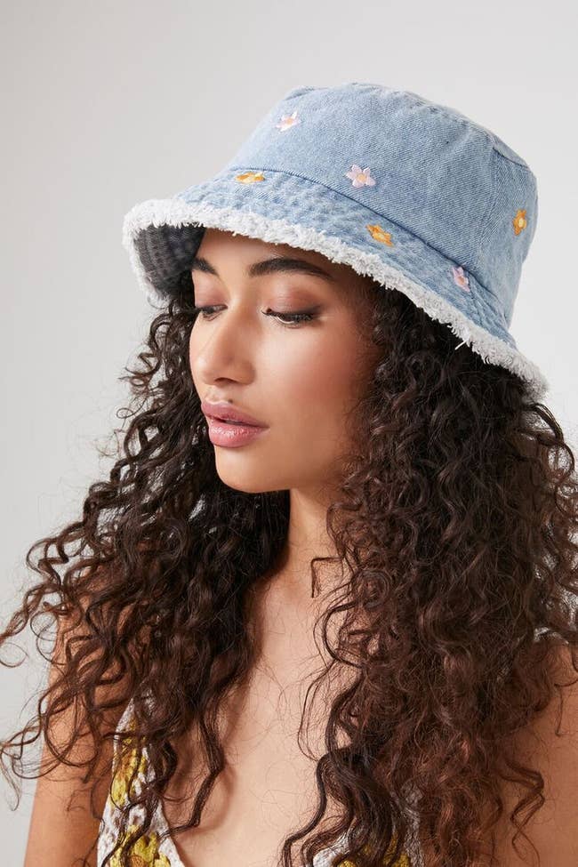 model in raw edge denim bucket hat with pink and orange embroidered flowers