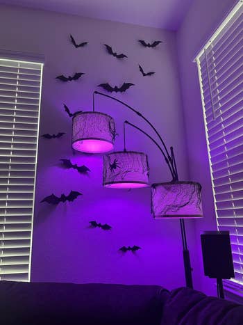 Stylish level  lamp with 3  shades, draped successful  netting, emits purple glow. Bat decorations screen  the adjacent    walls, creating a spooky vibe