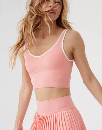 Woman in a pink crop top and pleated skirt smiling with her hair in motion