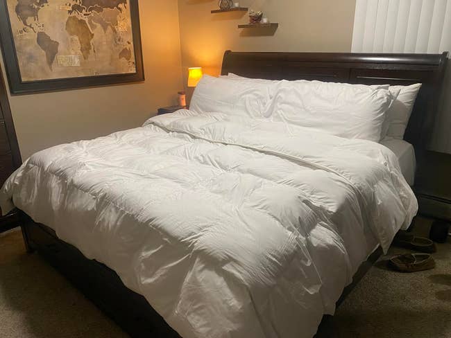 A neatly made furniture with a plush achromatic comforter successful a cozy chamber setting, featuring a satellite representation connected the partition and a softly lit lamp