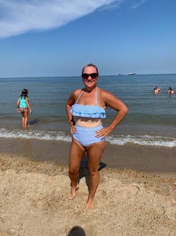 Woman in a ruffled bikini poses confidently by the beach with people swimming in the background