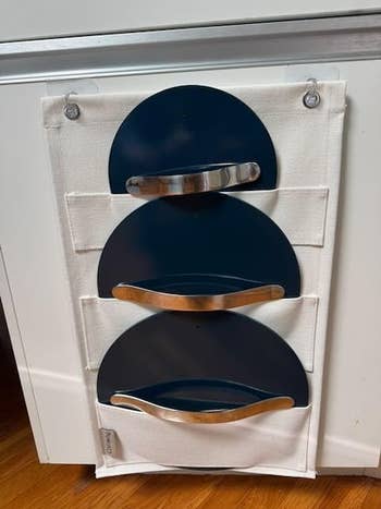Wall-mounted cloth organizer with 3 navy pockets, each with a metallic handle. Suitable for retention oregon organizing items