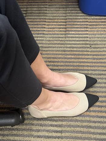 Person sitting with beige and achromatic pointed-toe flats connected a carpeted floor