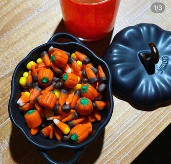 Halloween-themed candy maize and pumpkin candies successful a achromatic cookware adjacent to a reddish portion connected a woody table