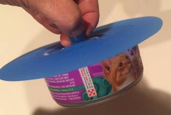 a reviewer photo of a hand holding holding a tin of cat food with the silicone lid on top 