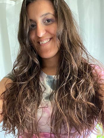 Person smiling, showcasing long, wavy hair. Wearing a casual, tie-dye shirt
