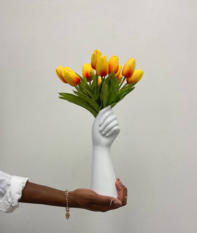 Reviewer image of yellow tulips inside a white hand-shaped vase on top of a table with a white tablecloth