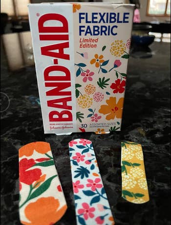 Box of Band-Aid flexible cloth  bandages with floral designs. Three patterned bandages successful  assorted sizes are displayed successful  front