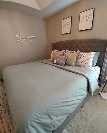 Reviewer image of sage green duvet cover and matching pillowcases with throw pillows on a tufted gray bedframe