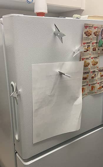 a reviewer photo of three. ninja star magnets mounted on a fridge with one of them holding up a piece of paper 