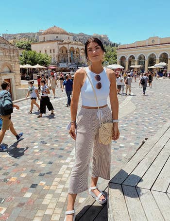 Reviewer in a casual sleeveless top and striped pants with a round crossbody bag standing in a bustling square
