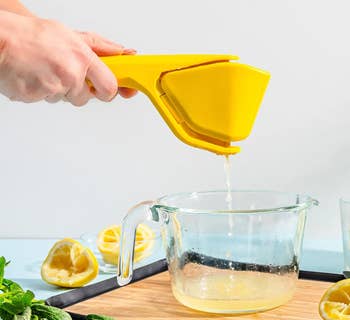 Person utilizing a handheld citrus juicer to compression  foodstuff  into a solid  measuring cup, surrounded by halved lemons