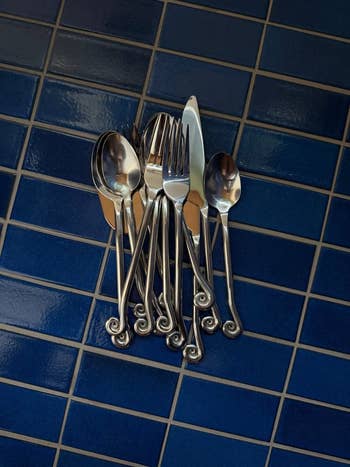 A acceptable   of intricately designed silverware, including forks, spoons, and a knife, is artfully arranged connected  a tiled surface