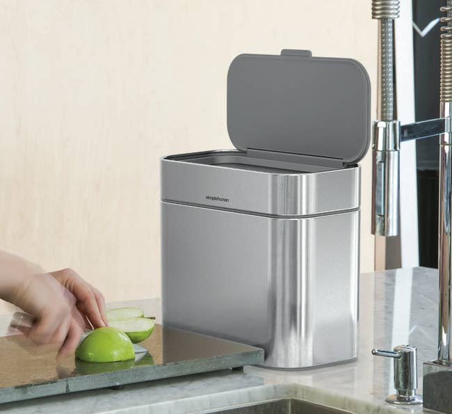 Stainless alloy trash tin with unfastened lid connected a room antagonistic adjacent a sink, beside sliced apples being chopped connected a cutting board