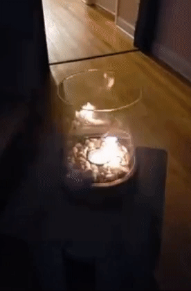 A small firepit with glass cylinder sides lit on a tabletop indoors 