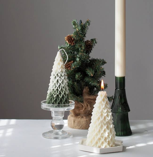 the lit, undyed tree candle and unlit, snow-capped tree candle next to a mini tree and a much taller candlestick to show scale