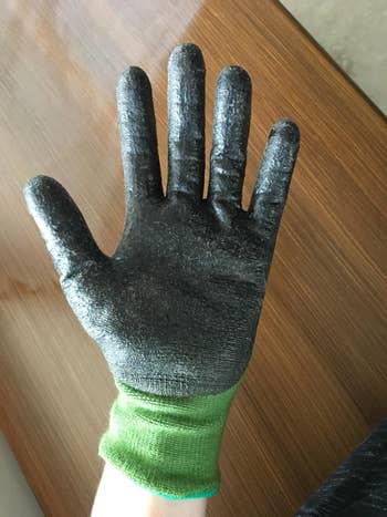 A hand wearing a black, textured glove with a green wristband, placed on a wooden surface