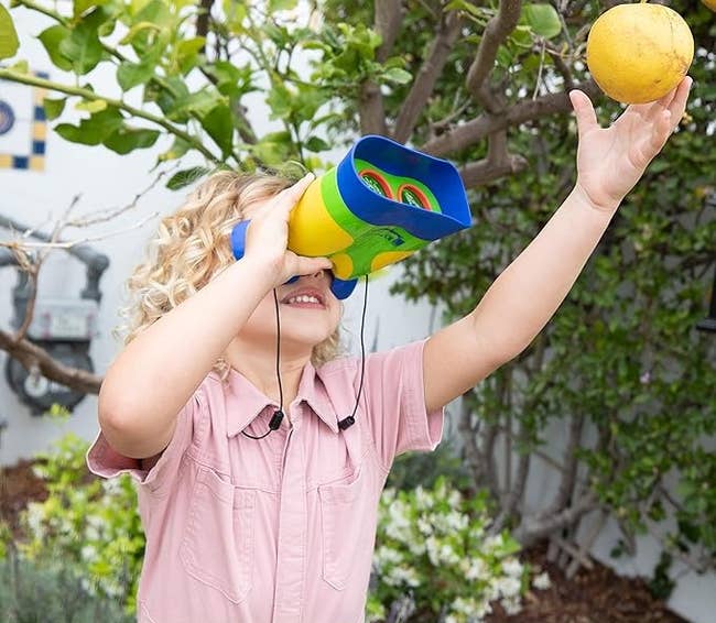 A child using the binoculars to look at a hanging fruit on a tree