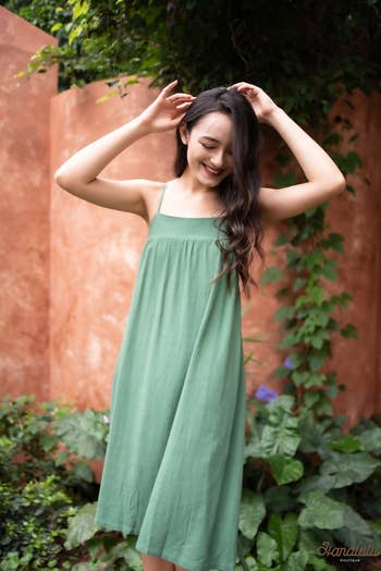 Woman in a casual green sundress smiling with hands in her hair, suitable for summer shopping