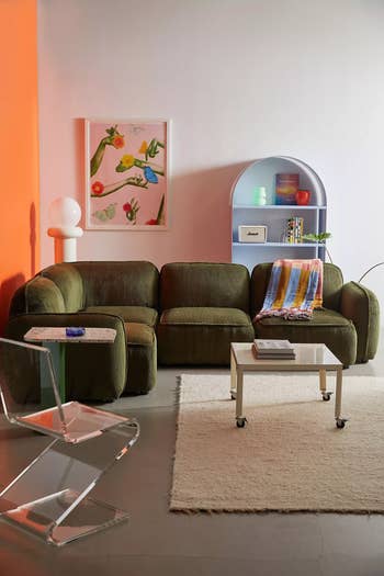 Stylish living room with a velvet couch, clear chair, modern art, and decorative shelf. Cozy and contemporary shopping inspiration