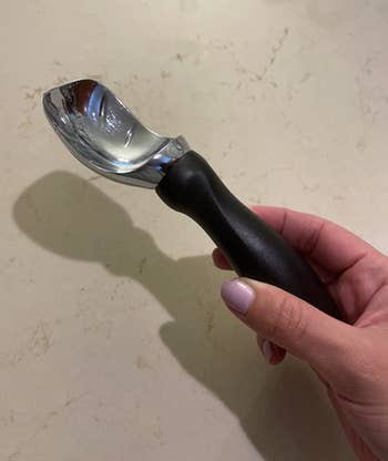 Reviewer holding black ice cream scoop with thick handle 