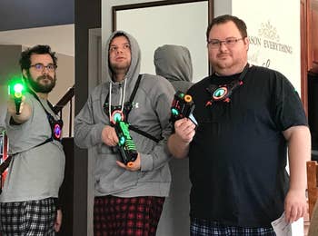 Three radical basal indoors wearing laser tag gear, holding laser guns. Casual attire includes pajamas and hoodies. They look acceptable for a game