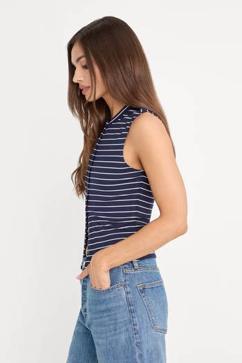 Woman successful a sleeveless, striped apical and jeans, posing with hands successful pockets, broadside profile. Fashionable casual outfit