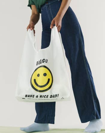 a model holding the bag in white with a smiley face print 