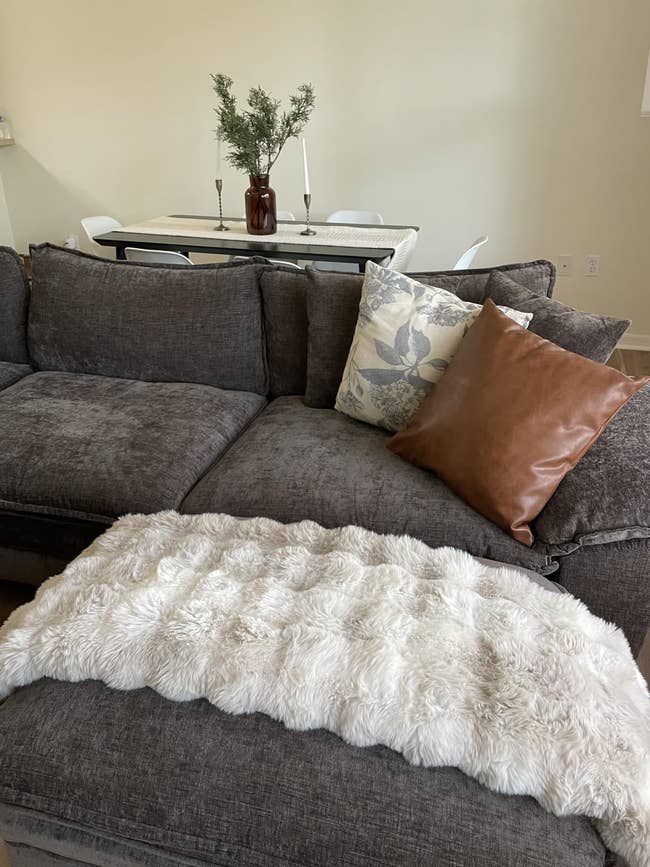 Cozy surviving country country with a plush grey sofa, 2 decorative cushions, and a fluffy achromatic throw. A eating array with chairs is successful the background