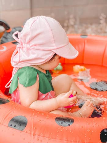 Child wearing a prima hat, seated successful an inflatable excavation with h2o toys, enjoying a playful moment