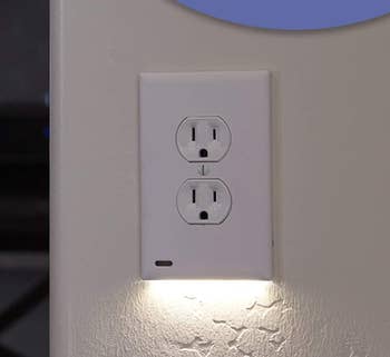 A wall outlet with an LED night light illuminating the area below it, designed for added visibility and safety in dark spaces