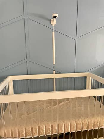 White modern baby crib with a breathable mesh mattress and a baby monitor mounted on the wall above