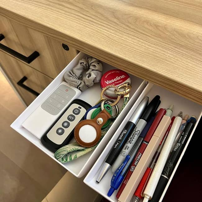 reviewer's two white drawers with pens, keys, and other supplies stored in them while installed under their desk 