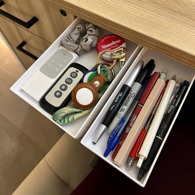 reviewer's two white drawers with pens, keys, and other supplies stored in them while installed under their desk 