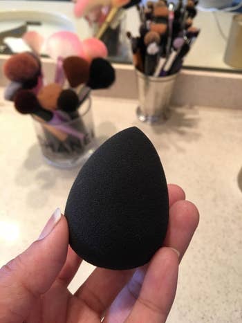 Reviewer holding a black beauty sponge with makeup brushes in background