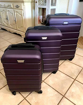 Reviewer photo of the three piece luggage set in purple with luggage handles down