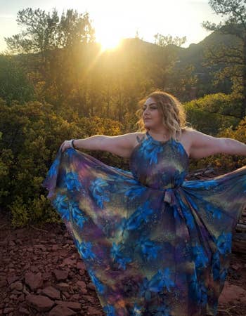reviewer in a flowing floral dress posing in nature at sunset
