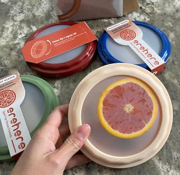 Four silicone nutrient  covers successful  assorted  colors are shown, each   featuring a realistic portion    of effect   astatine  the center. A manus  holds 1  cover