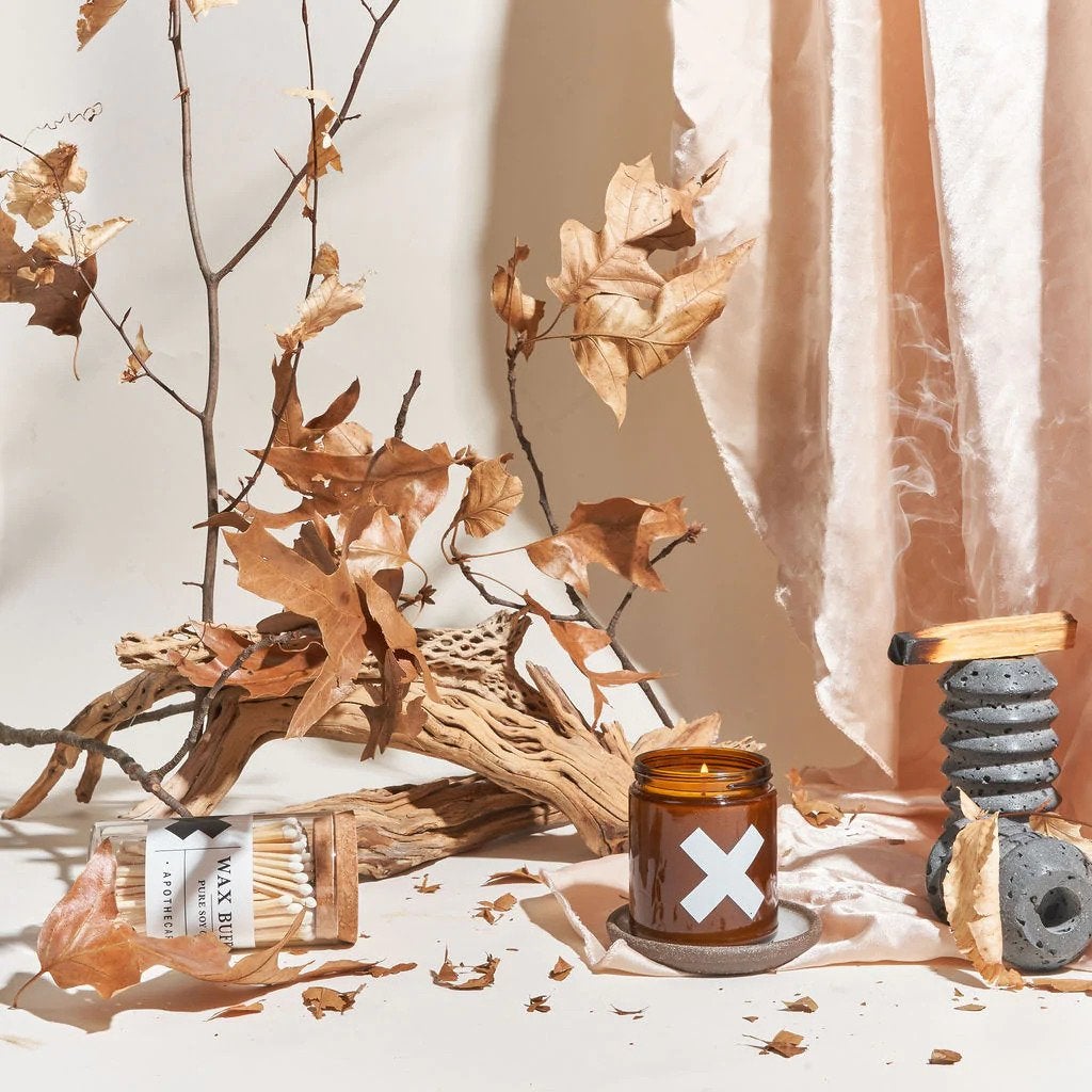 lit candle in amber glass jar beside matches driftwood and leaves 
