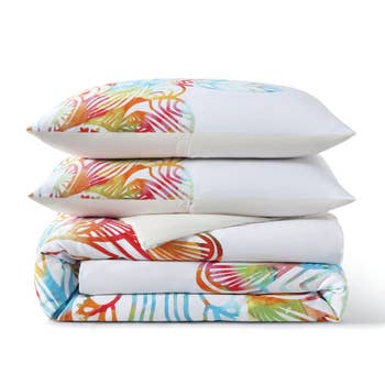 Stacked bed linens with vibrant tropical patterns, featuring a folded duvet cover and three pillows